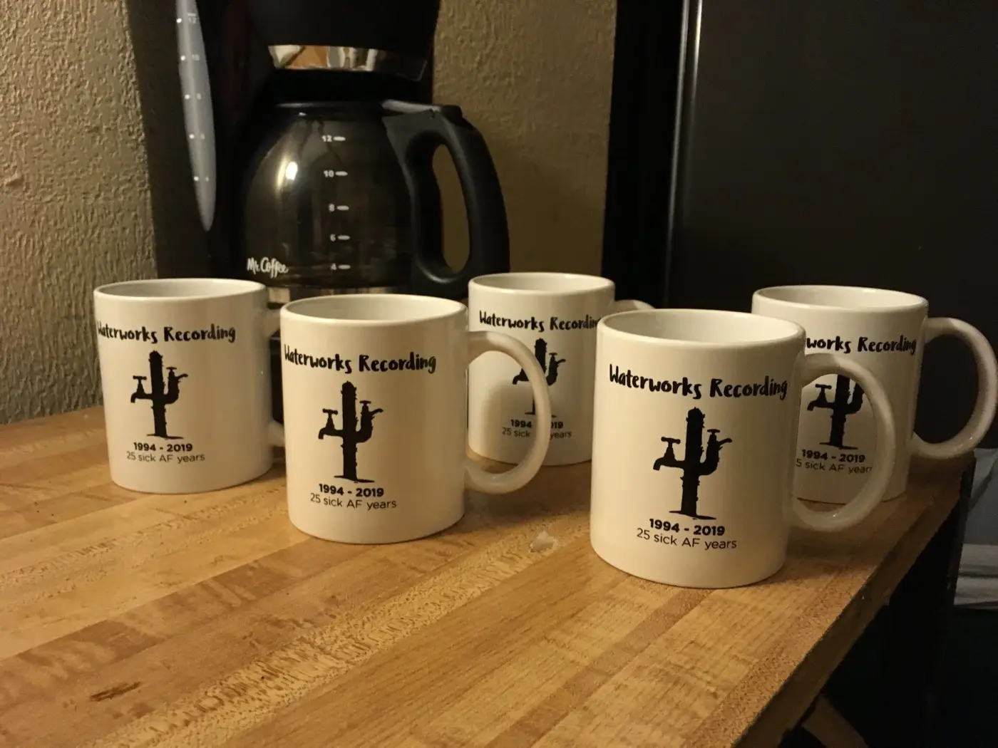 Five white coffee mugs next to a Mr. Coffee, each printed with the Waterworks Recording cactus-faucet logo and 1994 to 2019, 25 sick AF years.